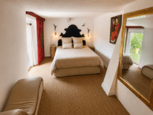 Queen bed with a black ornate headboard, beige bedding, and matching pillows; warm wall lamps and wooden nightstands flank it on white walls