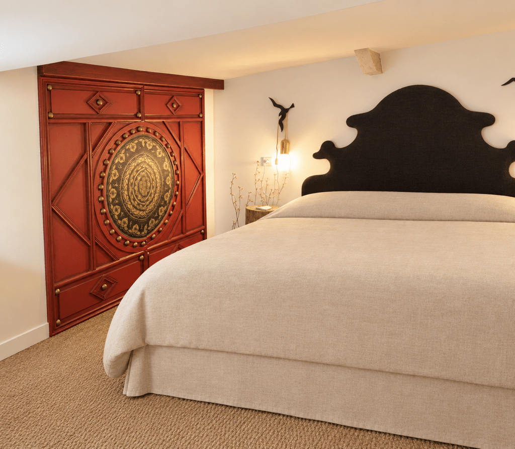 Bedroom with a large beige bed and a red ornate armoire featuring a gold circular mandala on the left, warm lighting nearby.